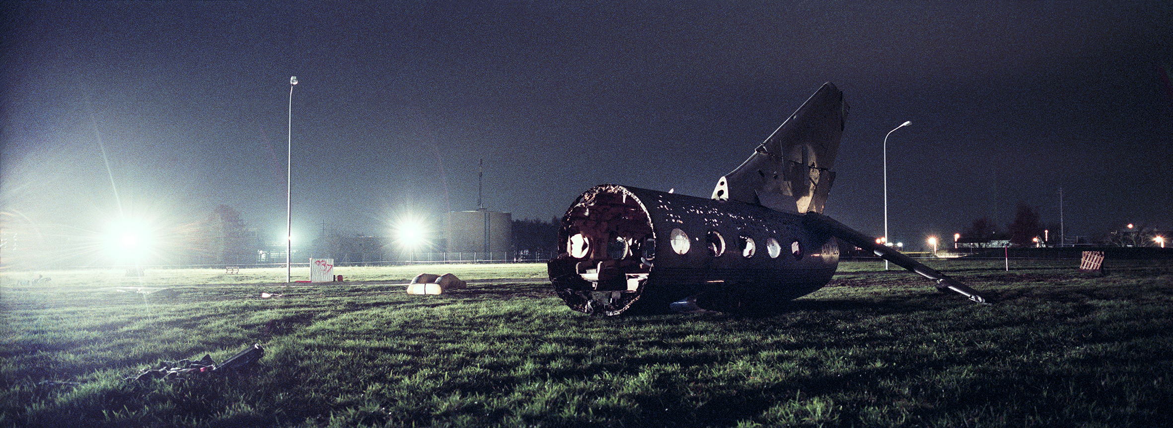 Teile eines Flugzeugrumfpes auf einer Wiese in der Nacht beleuchtet