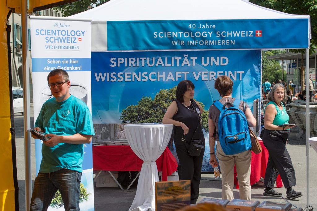 a man in blue scientology t-shirt in front of a info stand.