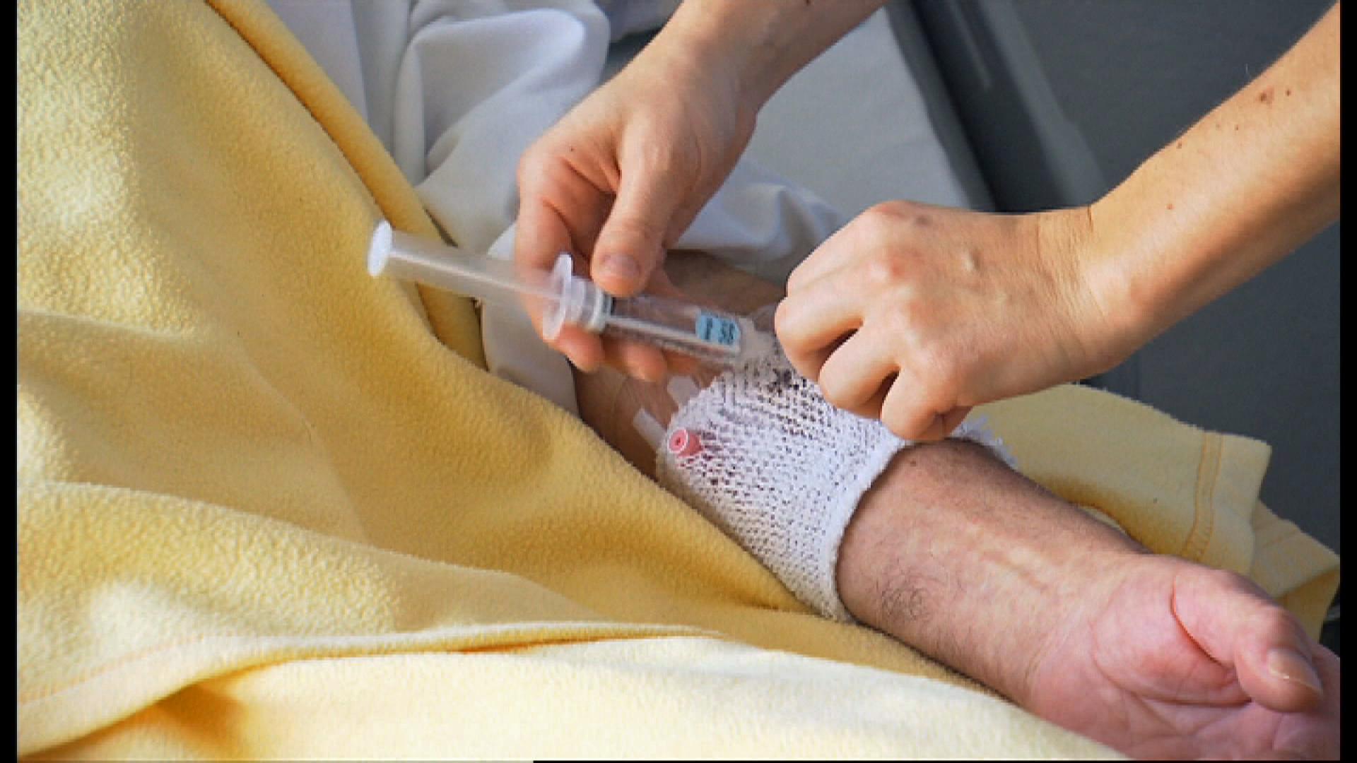 A pair of hands injecting a syringe into the forearm of an older person.