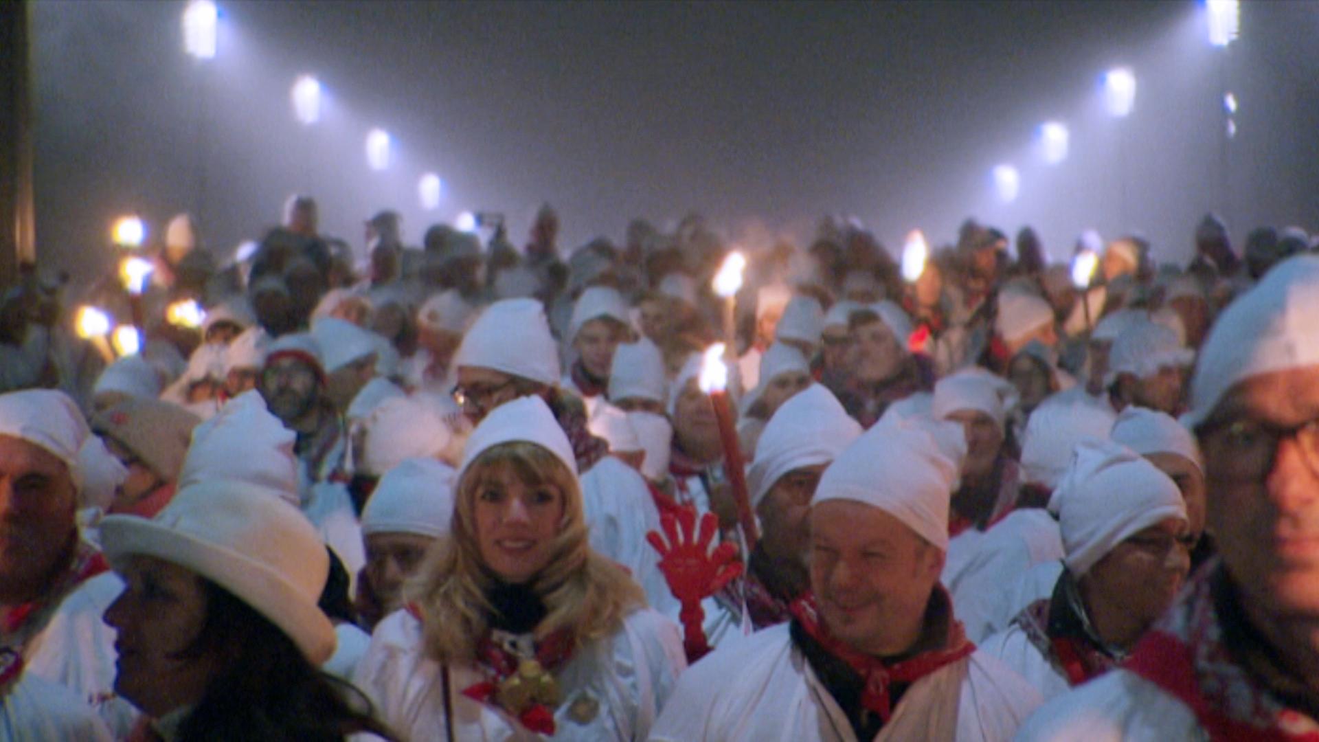 People in white nightshirts and -caps parade through the street of Solothurn opening the carnival season