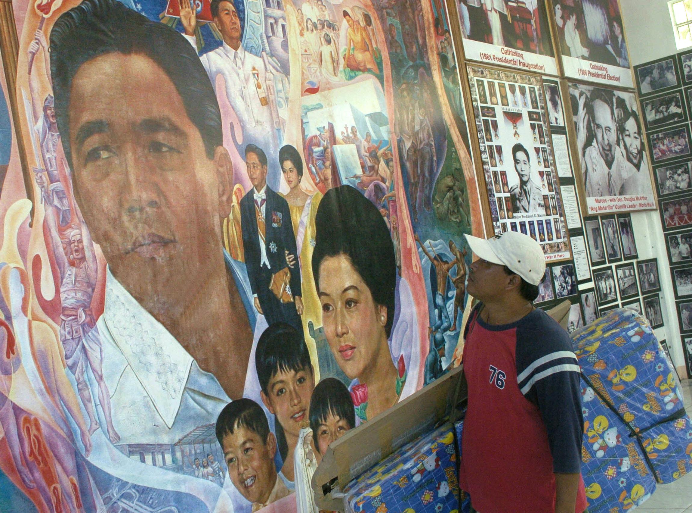 An ambulant bedding vendor looks at a giant mural of deposed former president Ferdinand Marcos at the family museum in the northern Philippines 30 September 2005.