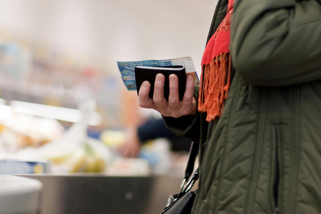 A hand holding a wallet and a 100 swiss franc bank note.