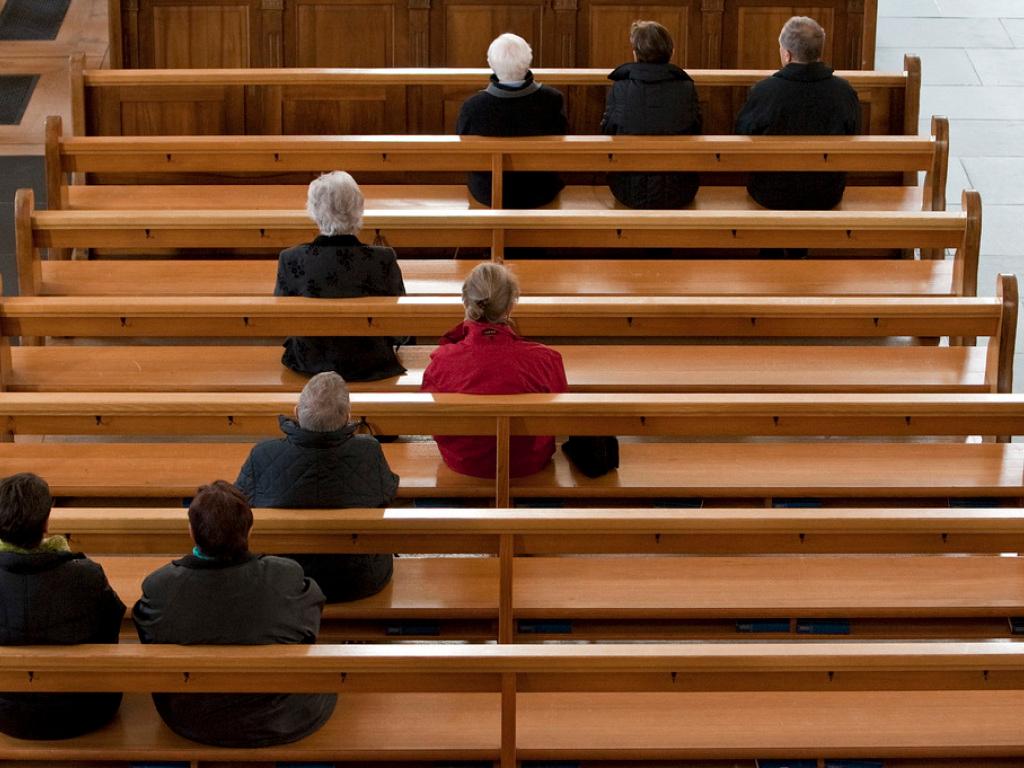 ganz wenige Menschen auf Holzbänken in einer Kirche