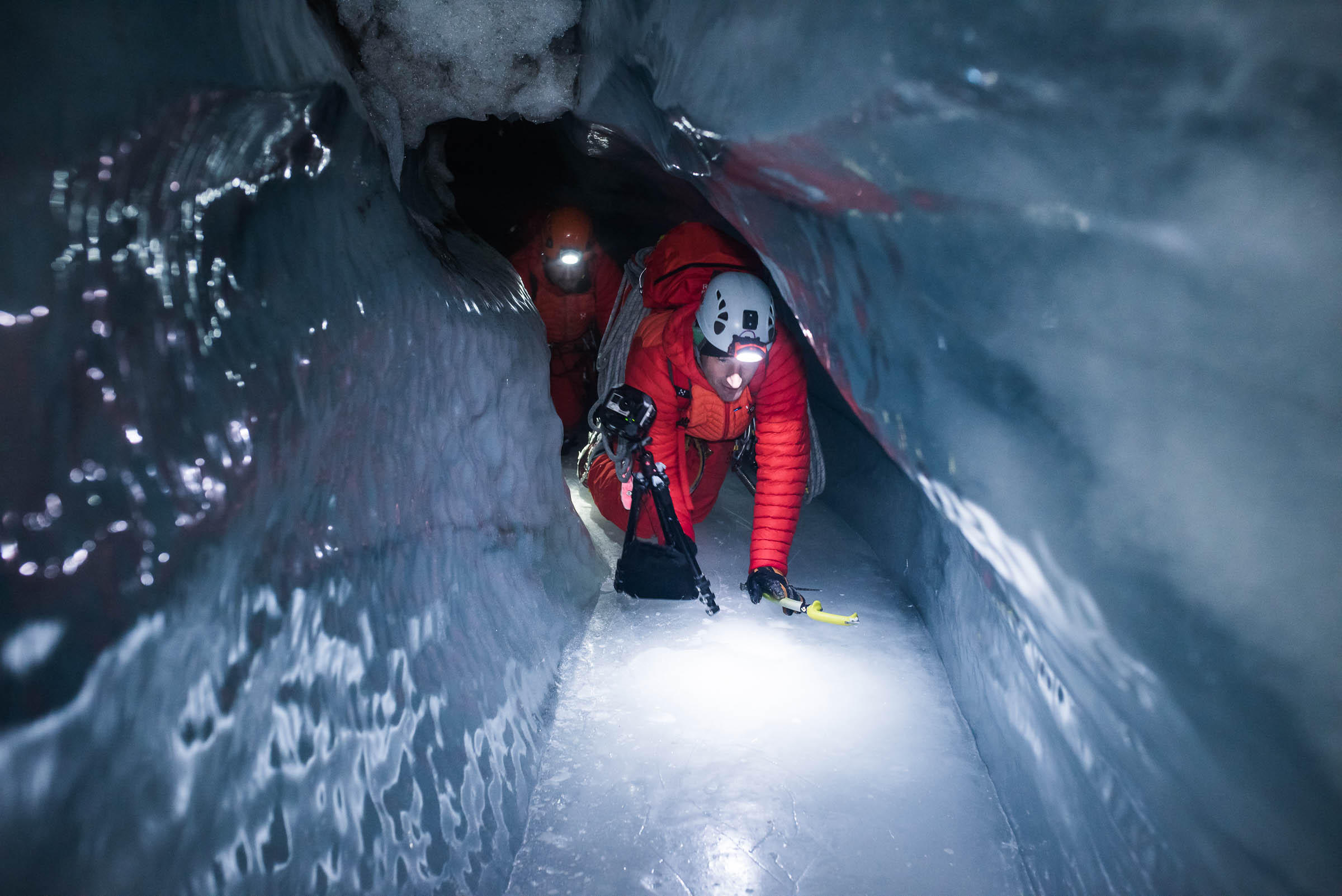 In narrow icy space, man with camera crawls on all fours