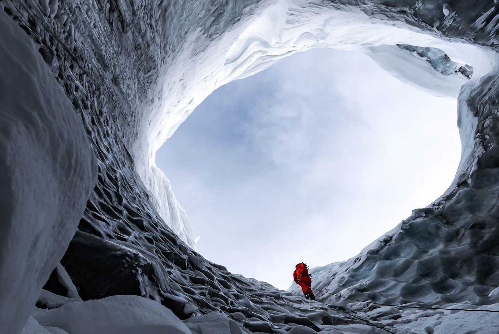 Seen from below, man stands at edge of large hole in glacier