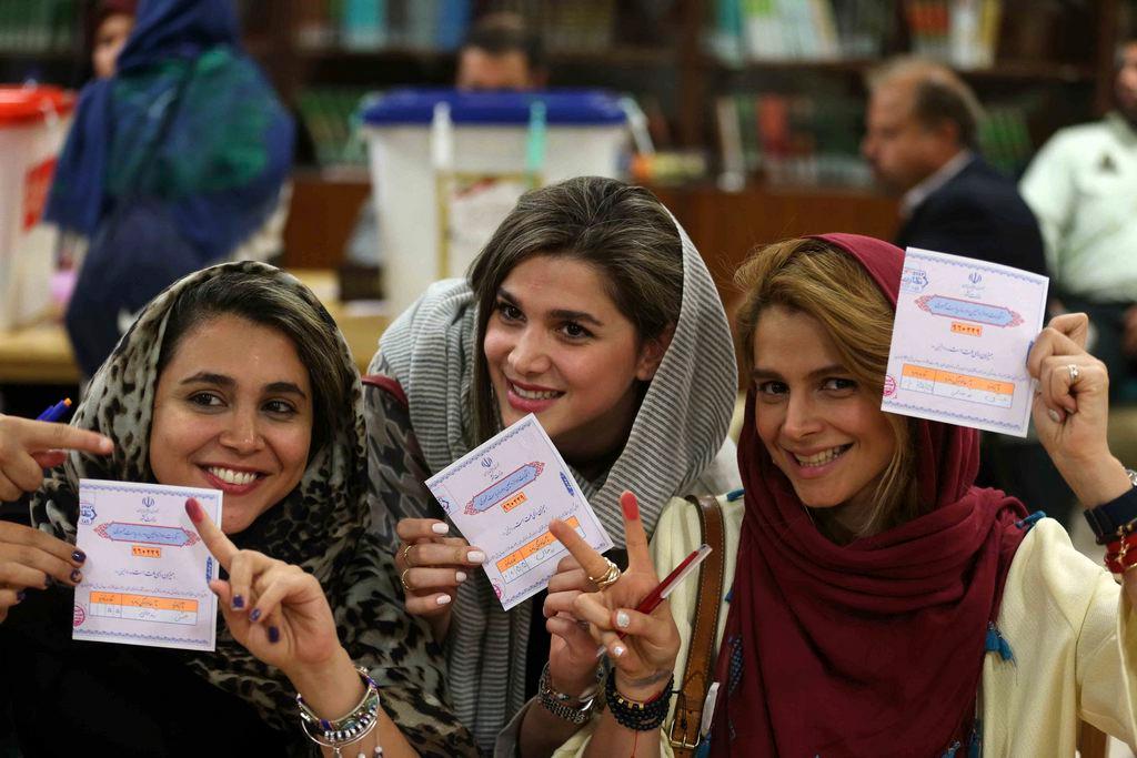 Drei lachende Frauen mit Kopfbedeckung zeigen ihre Wahlzettel.