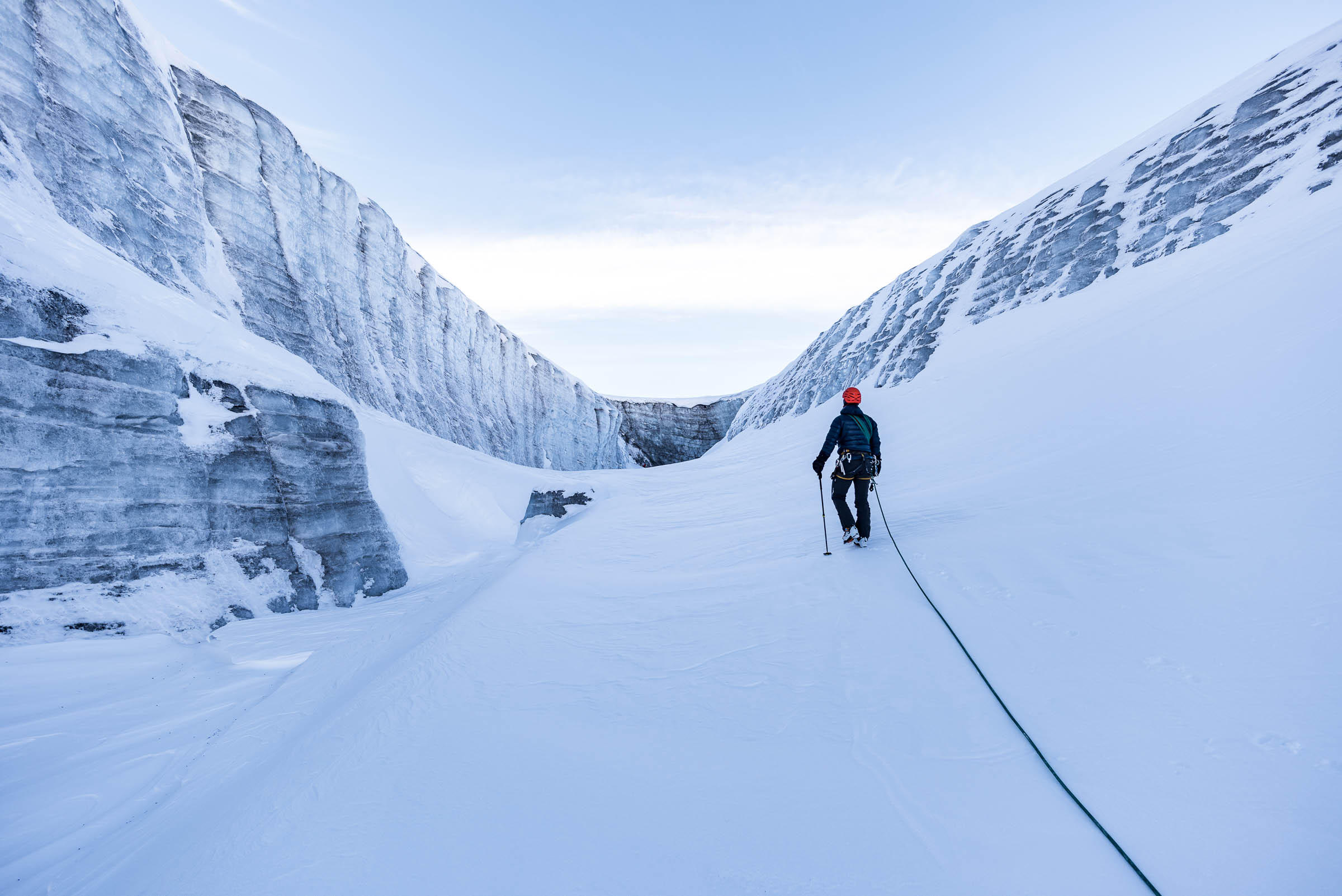 Man walks across snow-covered channel in glacier