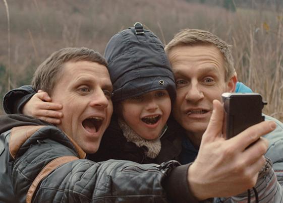 Zwei Männer und zwischen ihnen ein Junge machen ein Selfie.
