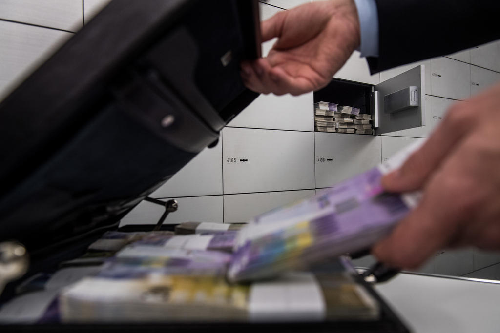 a man puts money in a suitcase in a room of bank safes