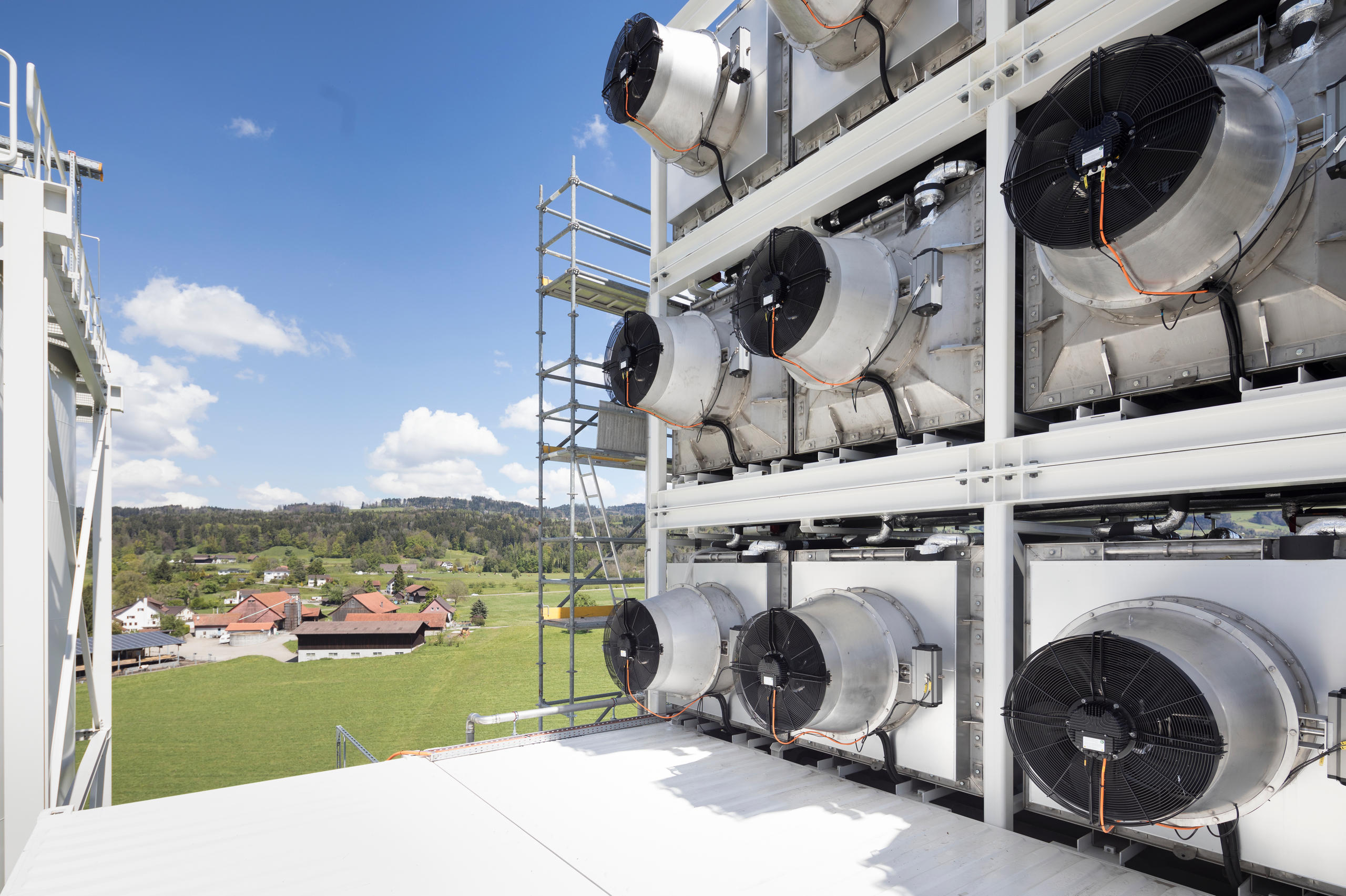 A machine that cleans the air of carbon dioxide with countryside and a farm in the background