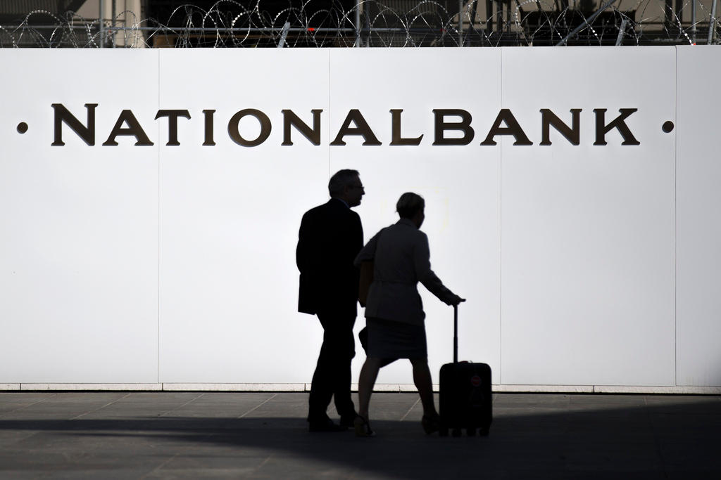Two figures are sillhoueted against a white Swiss National Bank sign