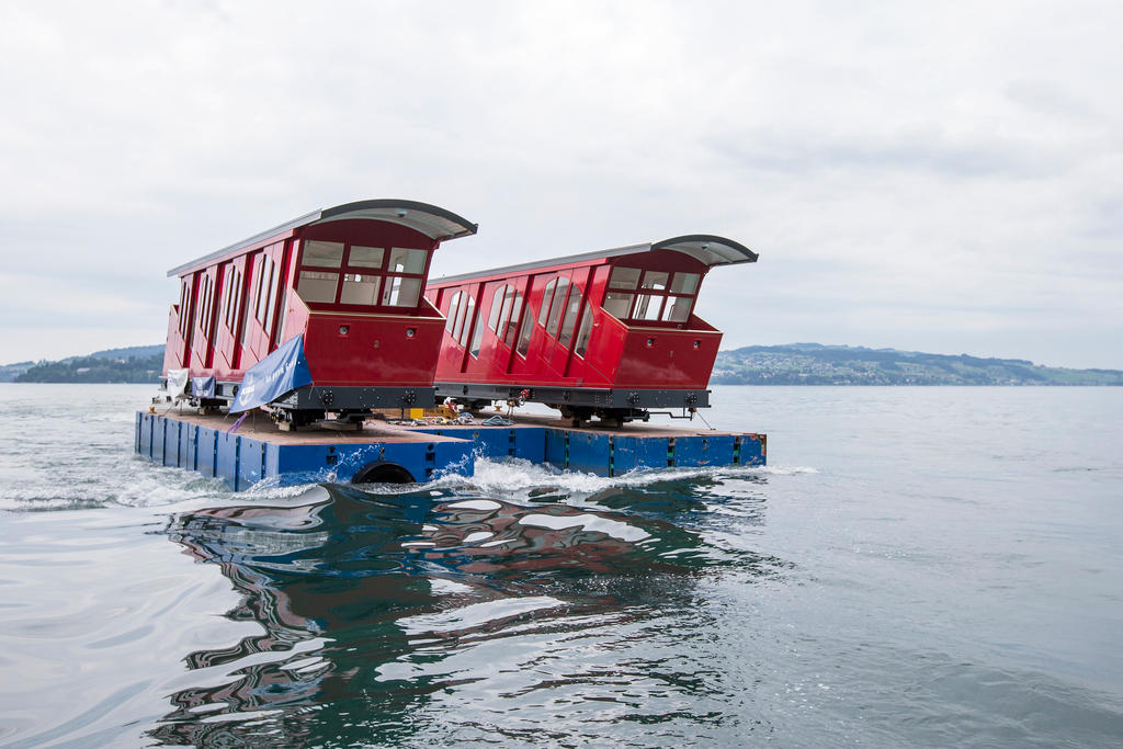 Dois vagões de funicular transportados em um pontão no lago
