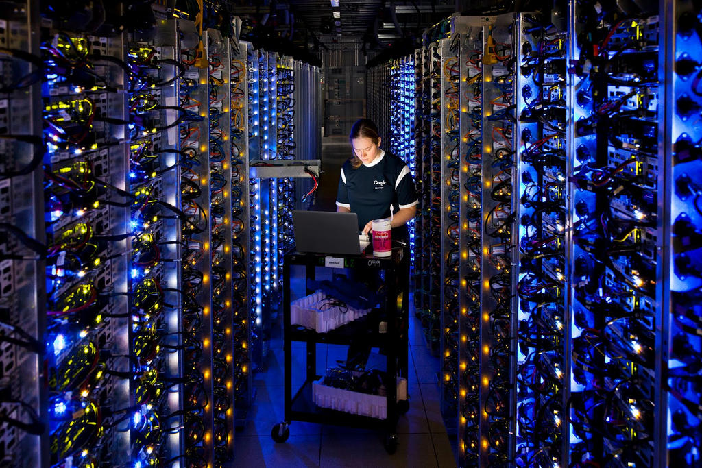 A woman kneels on the ground between rows of glowing computer processors.