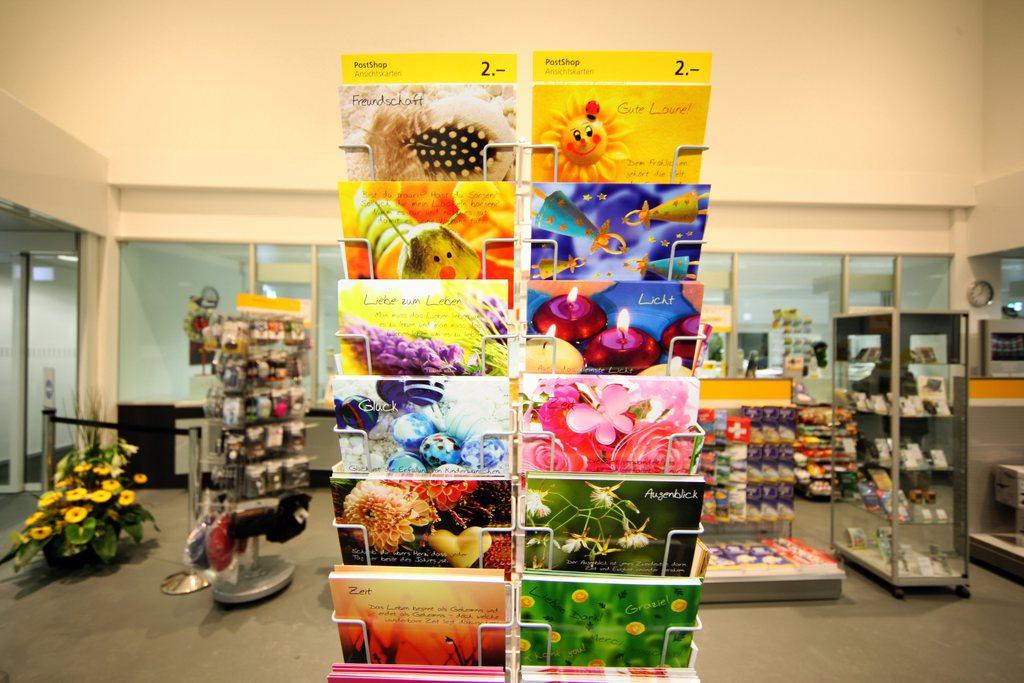 Nahaufnahme eines Postkartenständers in einer Postfiliale, im Hintergrund sind weitere Produkte zum Kauf zu sehen.