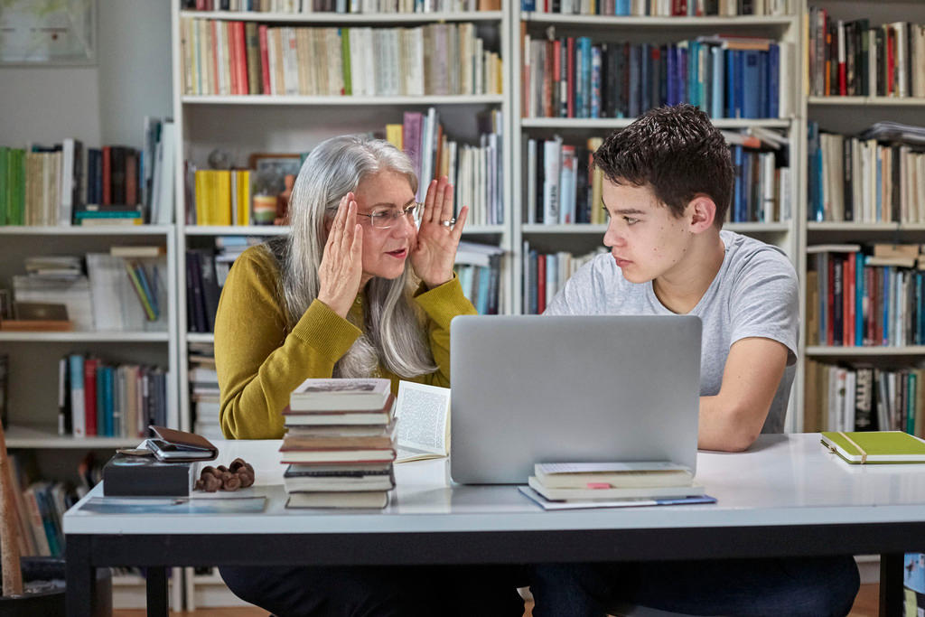Uma idosa com um jovem discutem frente ao computador em uma biblioteca
