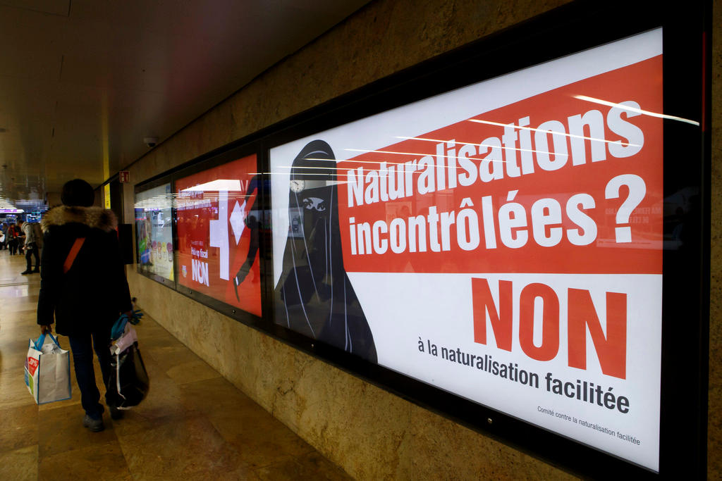 A person walks past a poster depicting a woman in a Burka, with the message No to uncontrolled naturalisation