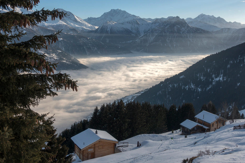 Three chalets overlook a cloud filled valley on a snowy hillside