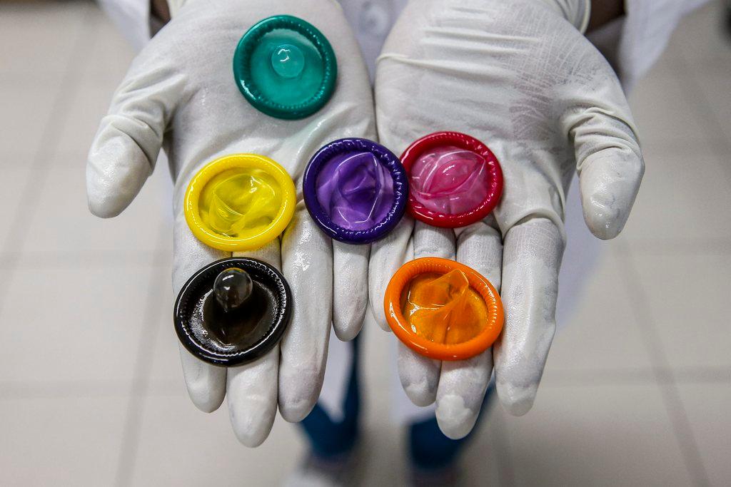 A person holds a variety of colored condoms in their palms.