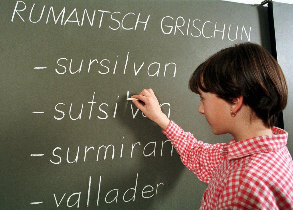 A schoolgirl writes in Romansh on a blackboard with chalk
