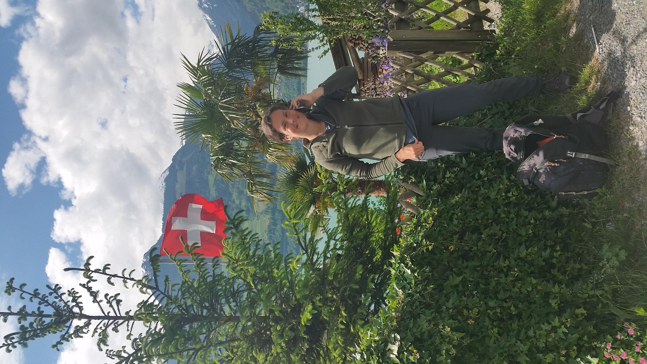 Alexandra Dufresne making a phone call in Switzerland, surrounded by trees and flowers.