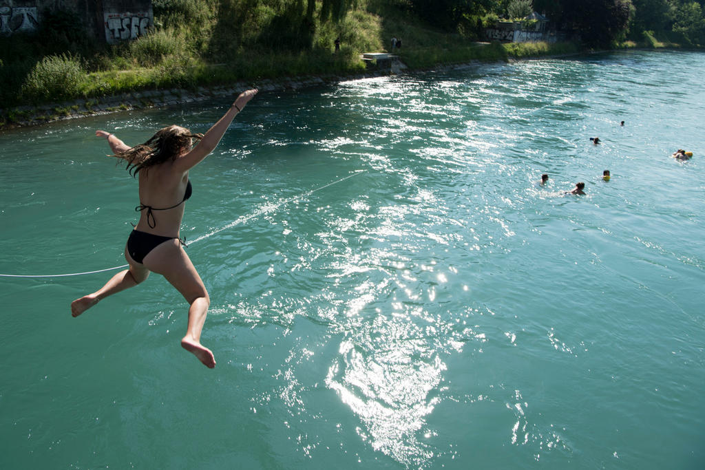 A woman in swimsuit jumps into a river to join other swimmers