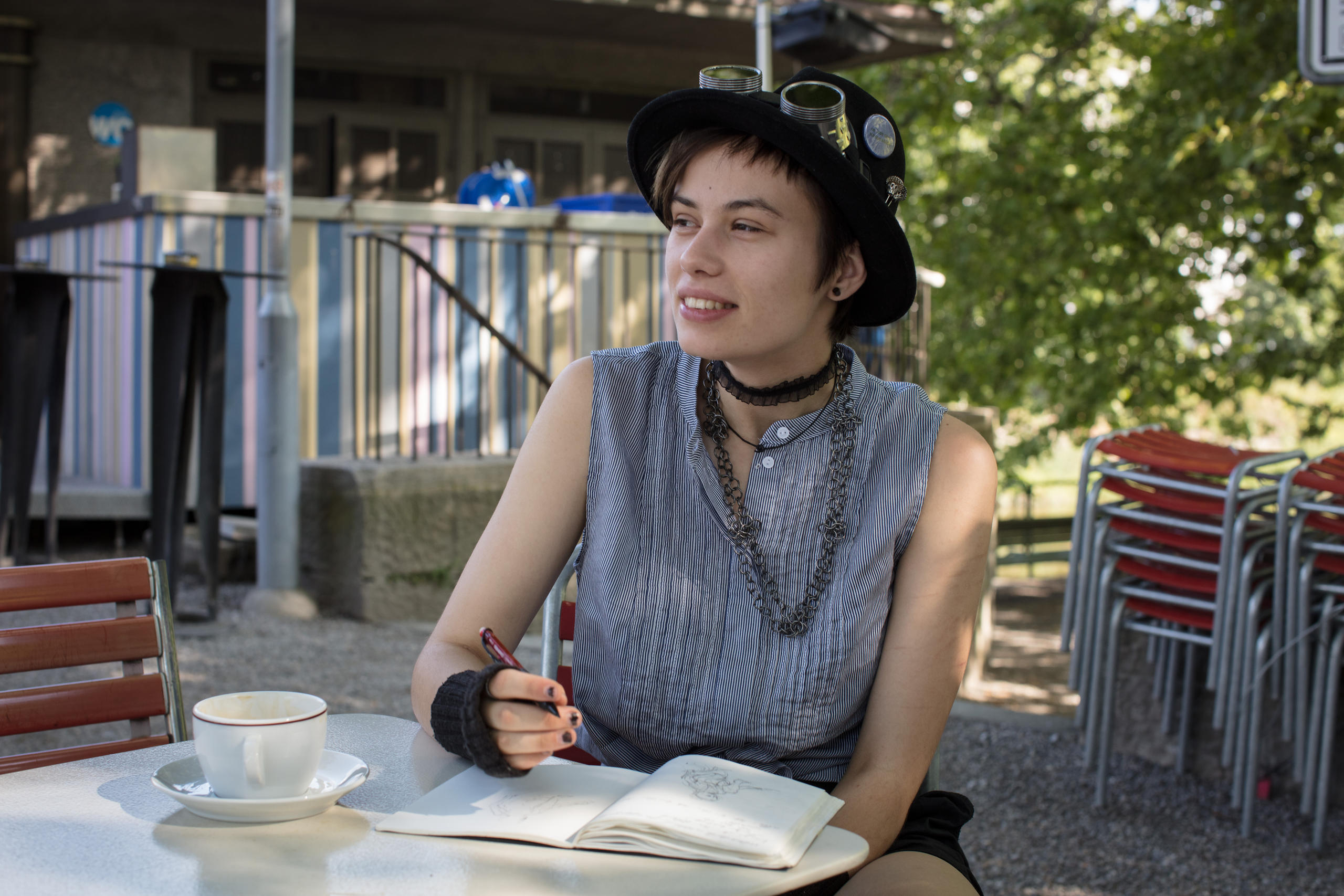 Runa Wehrli con sombrero sentada en una cafetería con un libro y un cafe.