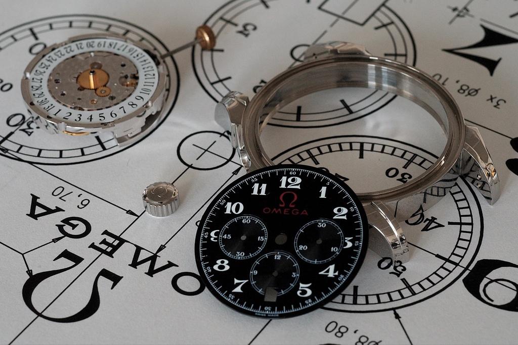 An Omega mechanical watch with a black watch face sits separated into constituent parts