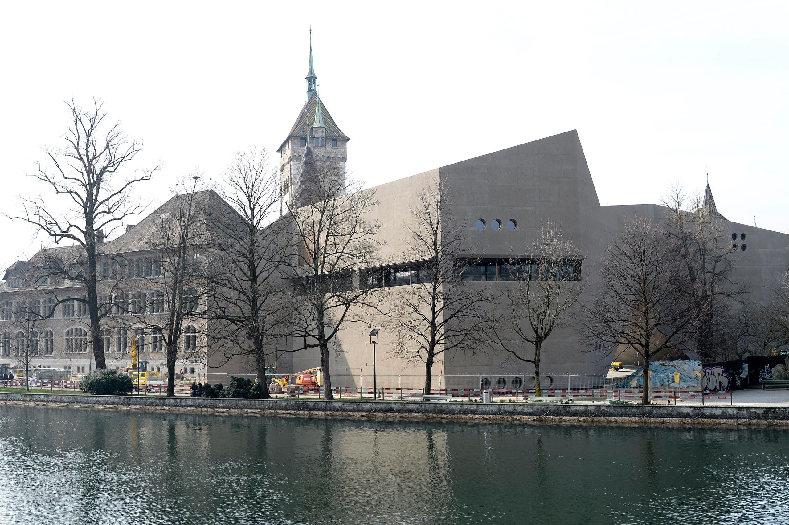 Moderner Betonblock vor einem romantischen Burgturm. Im Vordergrund ein Fluss.