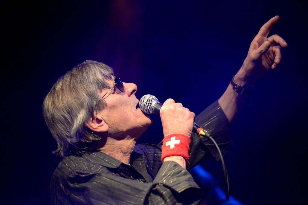 Polo Hofer, with a red wrist band sporting the Swiss cross, sings into a microphone on stage