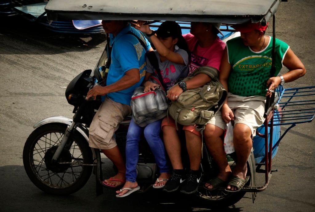 Filipinos ride on three-wheeled motorcycle on a street in Manila