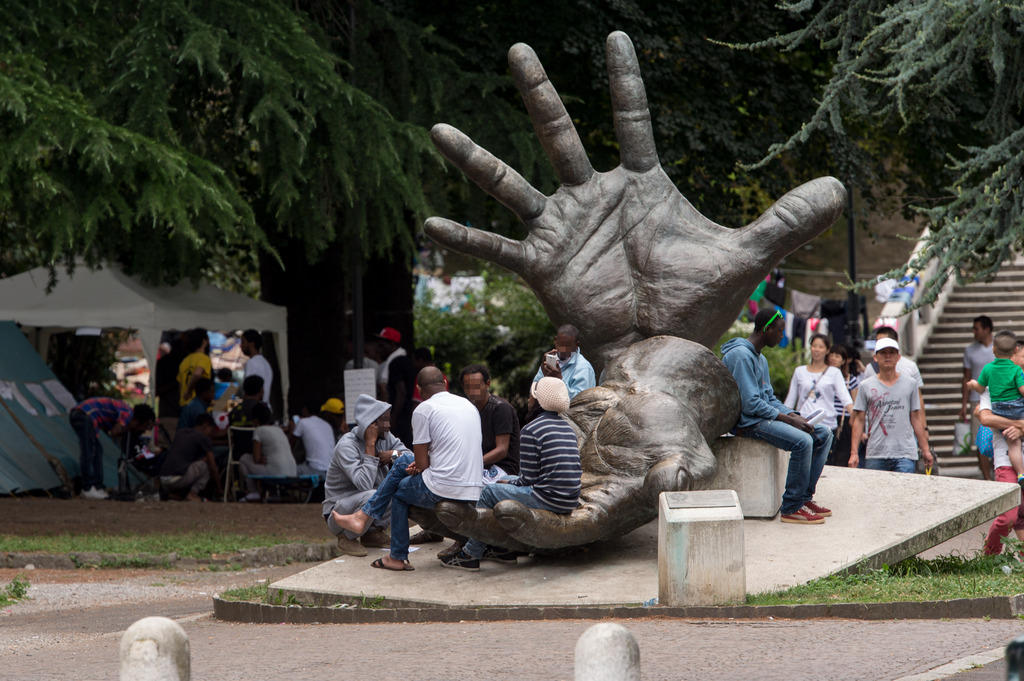 Migrants seated around a big sculpture of a hand sticking up in Como, Italy