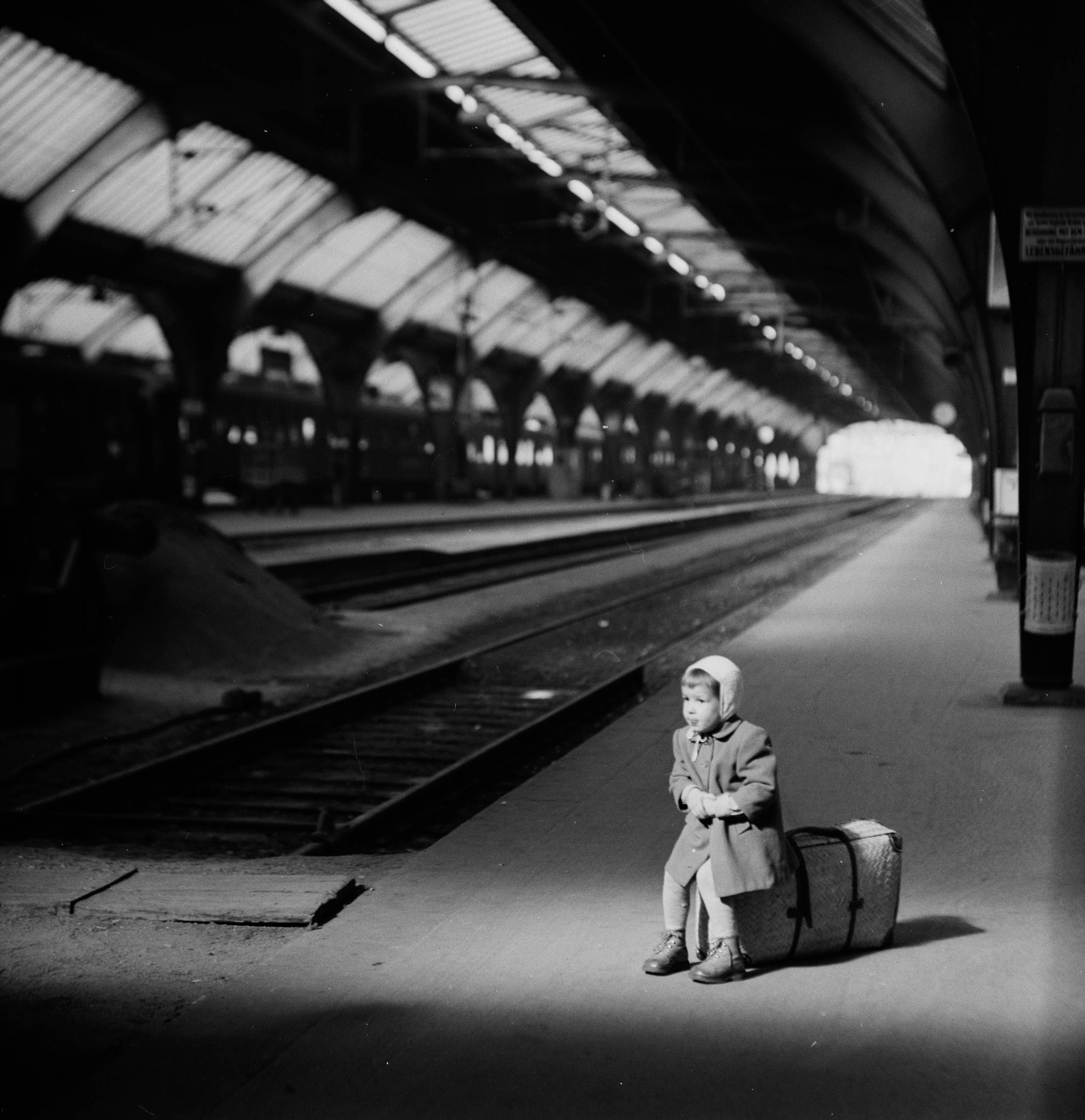 Un bambino seduto su una valigia alla stazione.