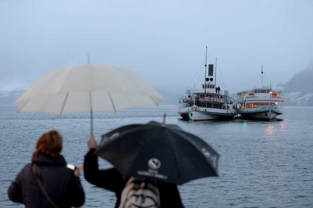 Touristen mit Regenschirmen blicken auf Passagierschiffe auf dem Vierwaldstättersee
