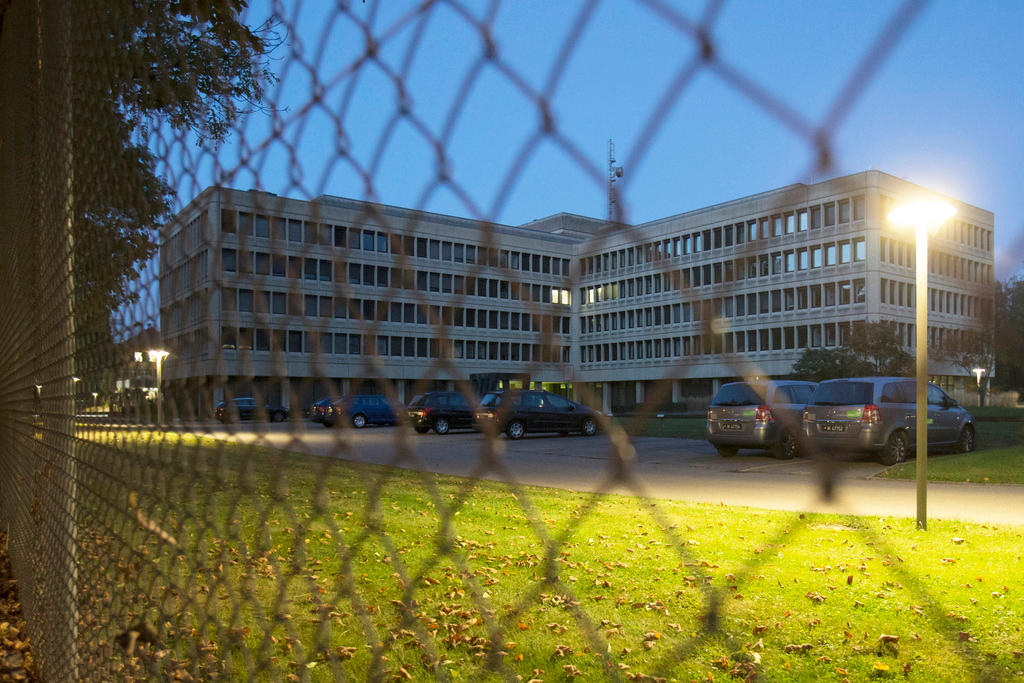 A large office block behind wire fencing is lit by a street lamp at dusk