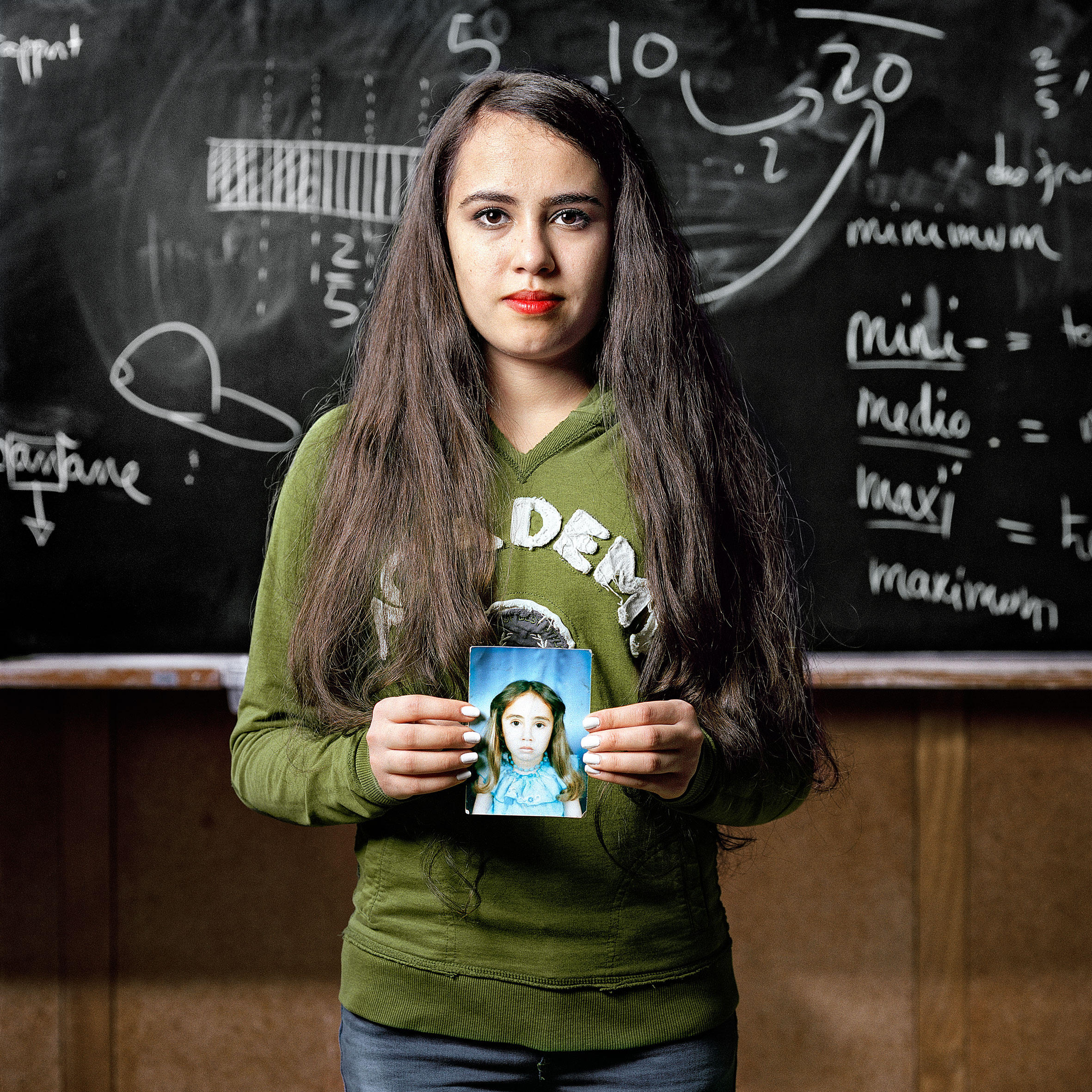 teenage girl stands in front of blackboard holding a photo