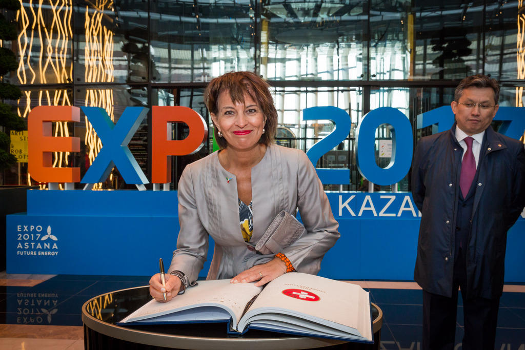 Doris Leuthard signs a book with the Expo 2017 sign in the background