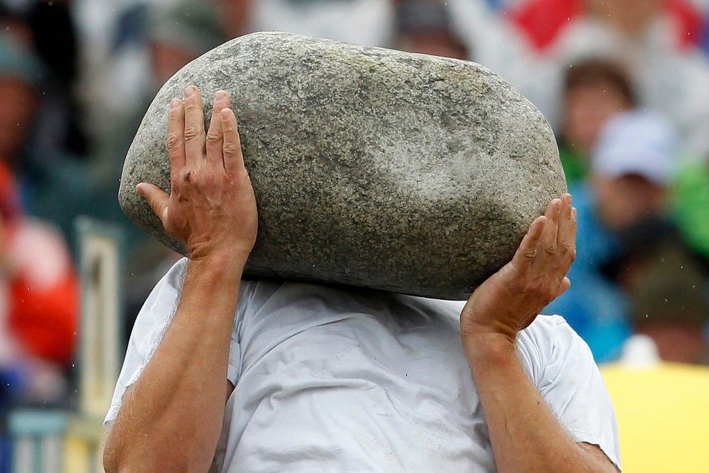A man holds a large stone over his face
