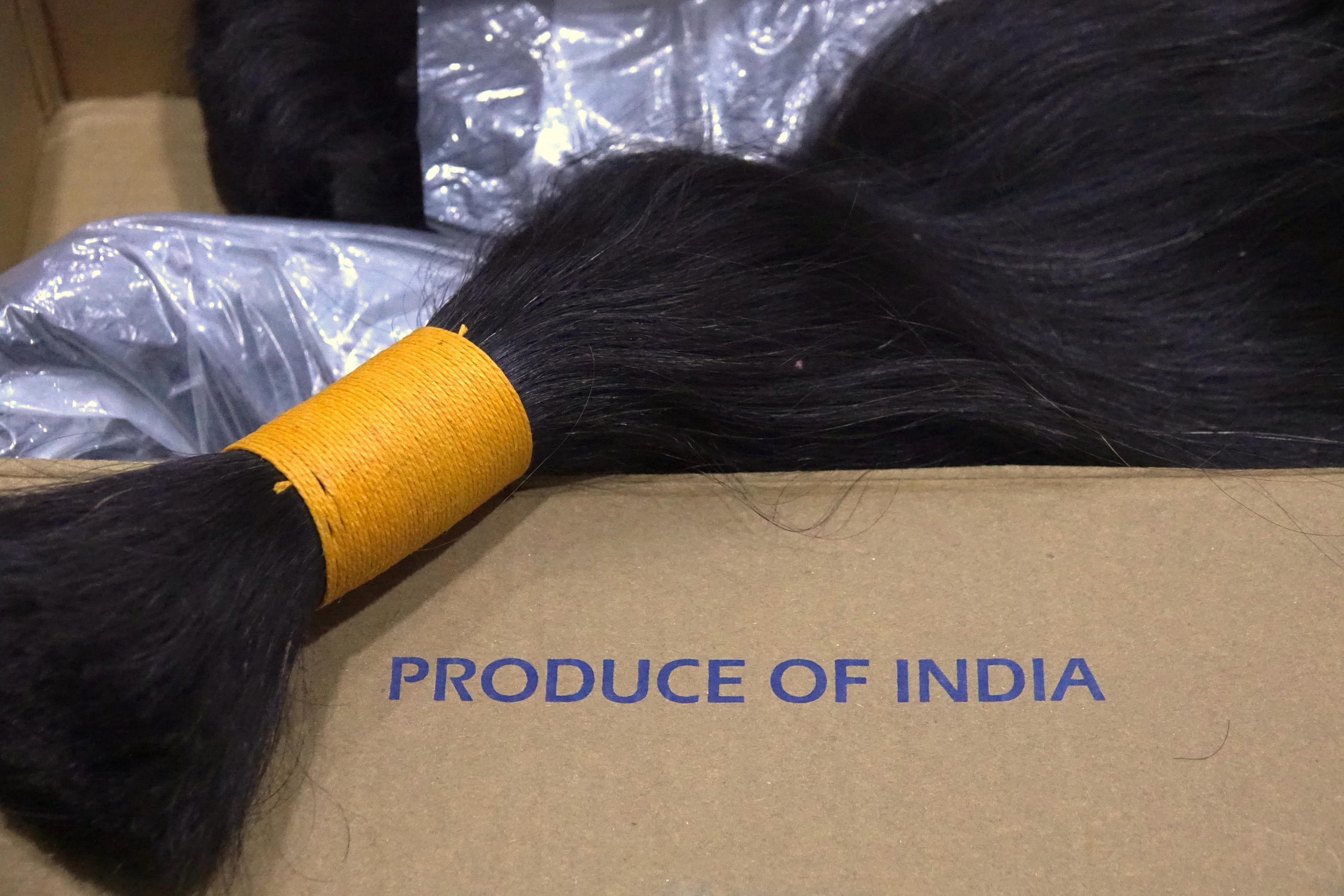 A lock of black hair bound with a yellow tie sits on a box marked Produce of India
