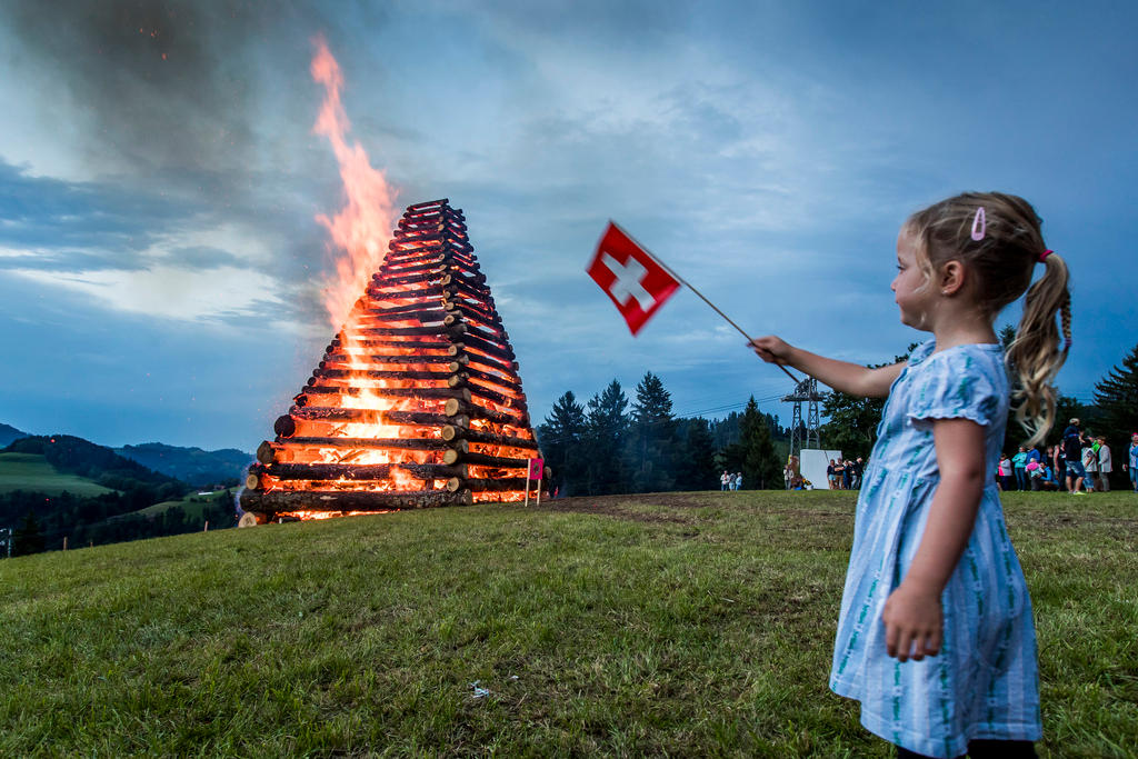 Fischenthal, Zurigo. Una bambina sventola una bandiera svizzera di fronte al falò per il 1° agosto, Festa nazionale.