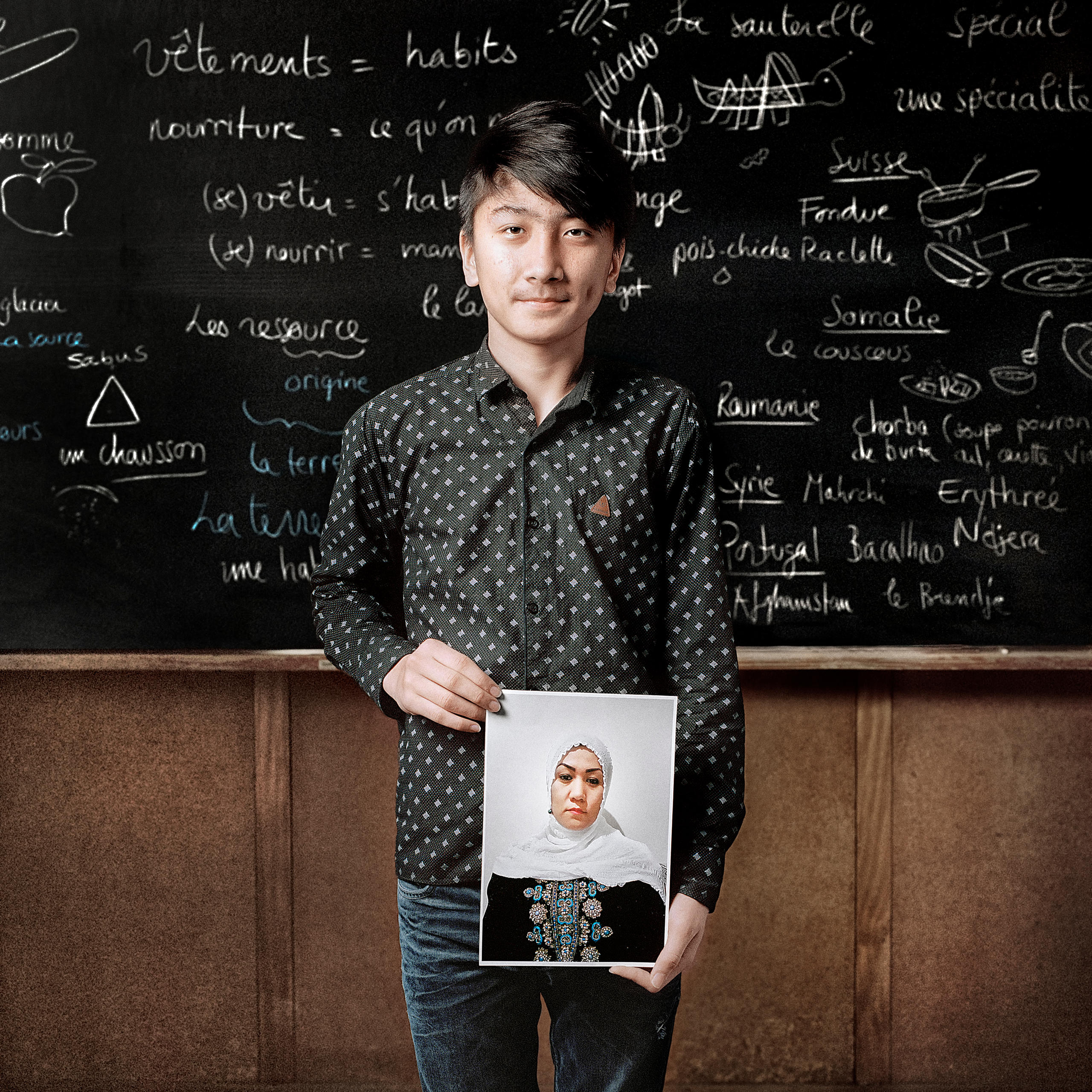teenager stands in front of blackboard holding a photo