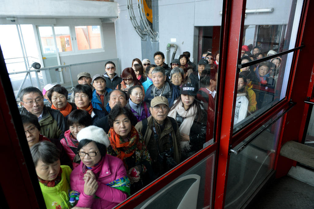 亚洲游客在铁力士山山脚下等待登山火车，上山的交通承载能力某种程度上间接调控了山上的游客的数量。