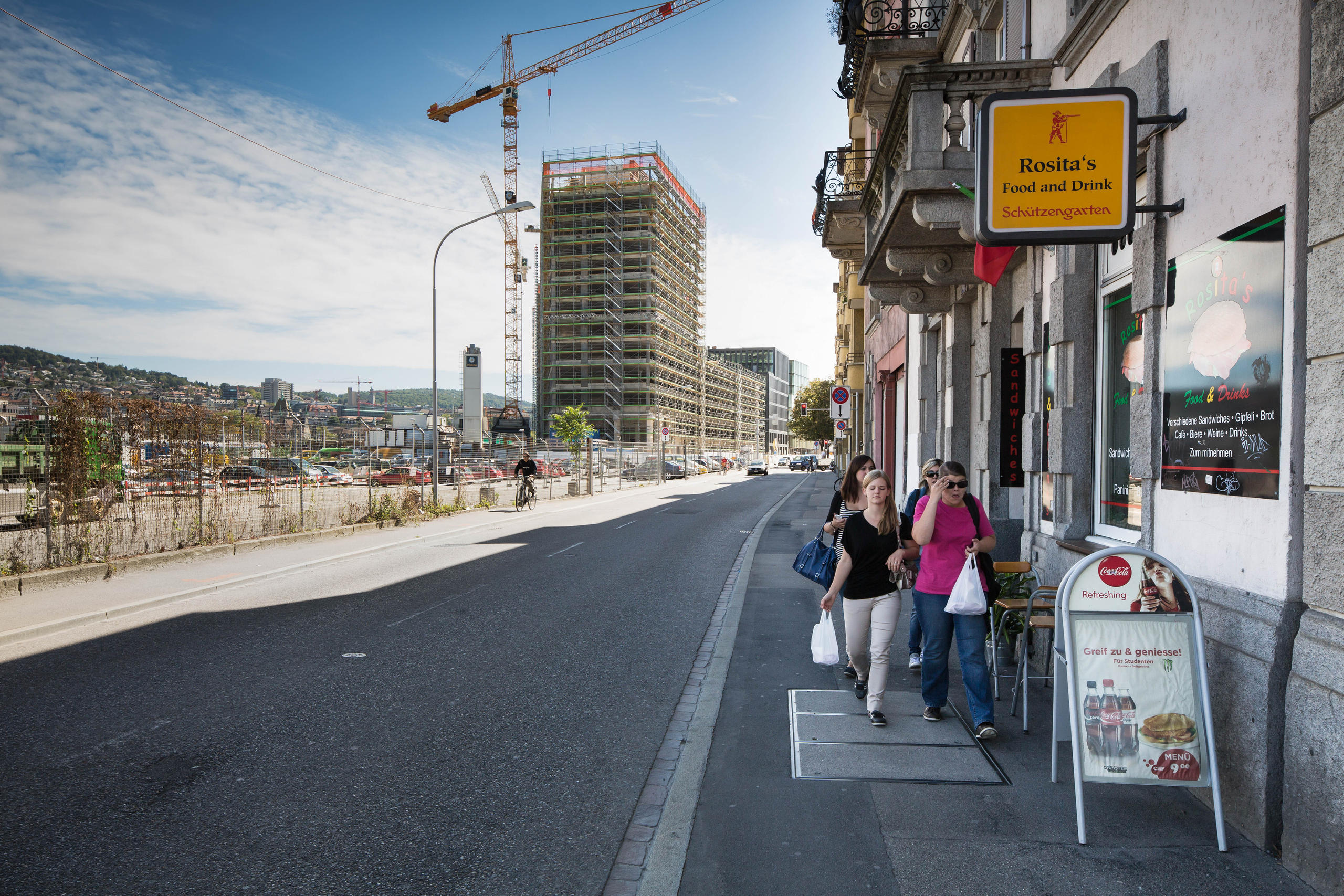 Menschen gehen auf Trottoir zwischen alten Gebäuden und Baustelle