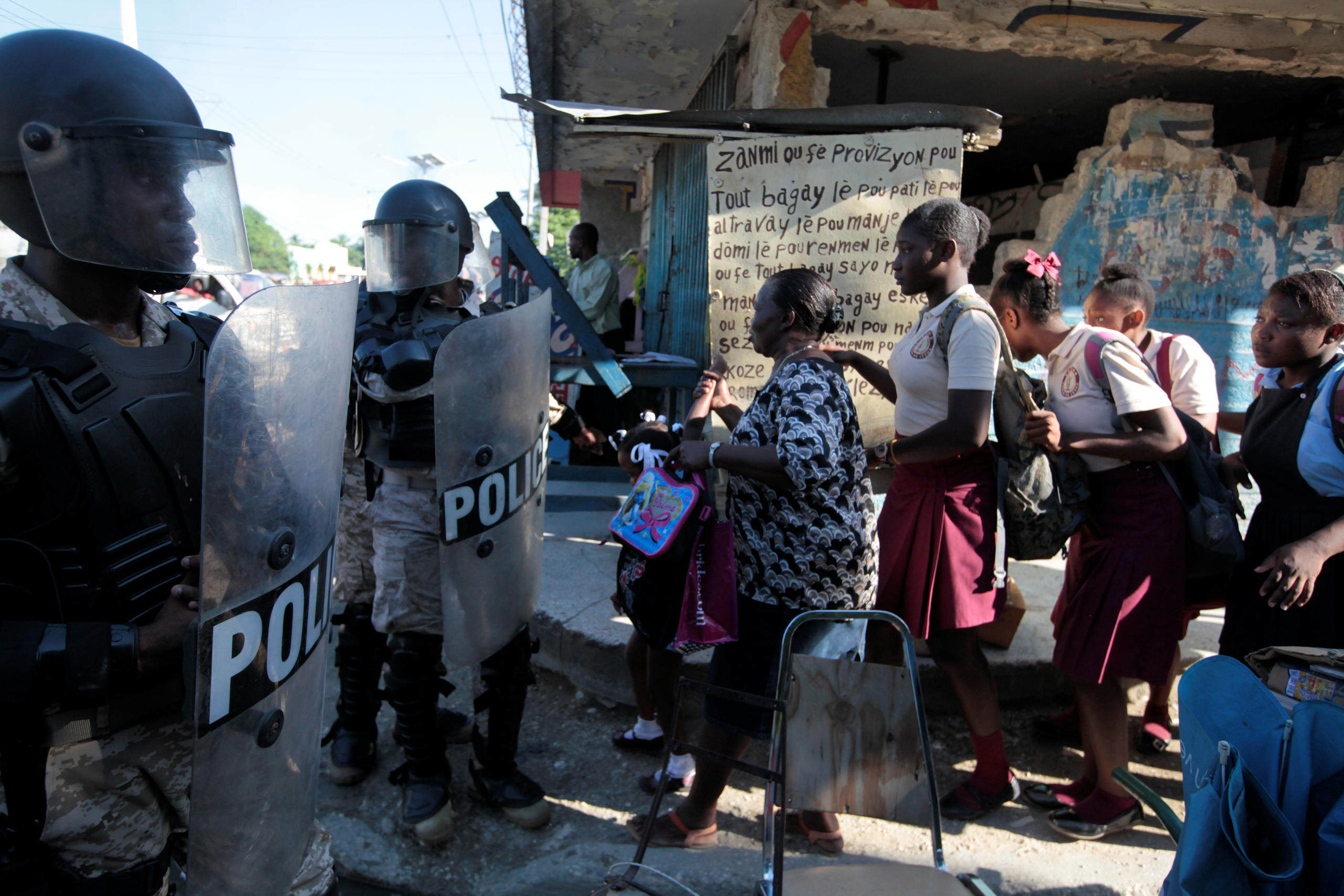 Eine Frau und Schulmädchen passieren eine Polizeiblockade in Haiti, nachdem Unruhen ausgebrochen sind.