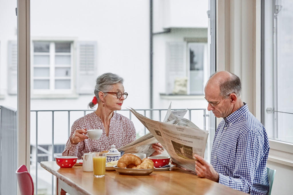 朝食をとりながら新聞を読む老夫婦の写真
