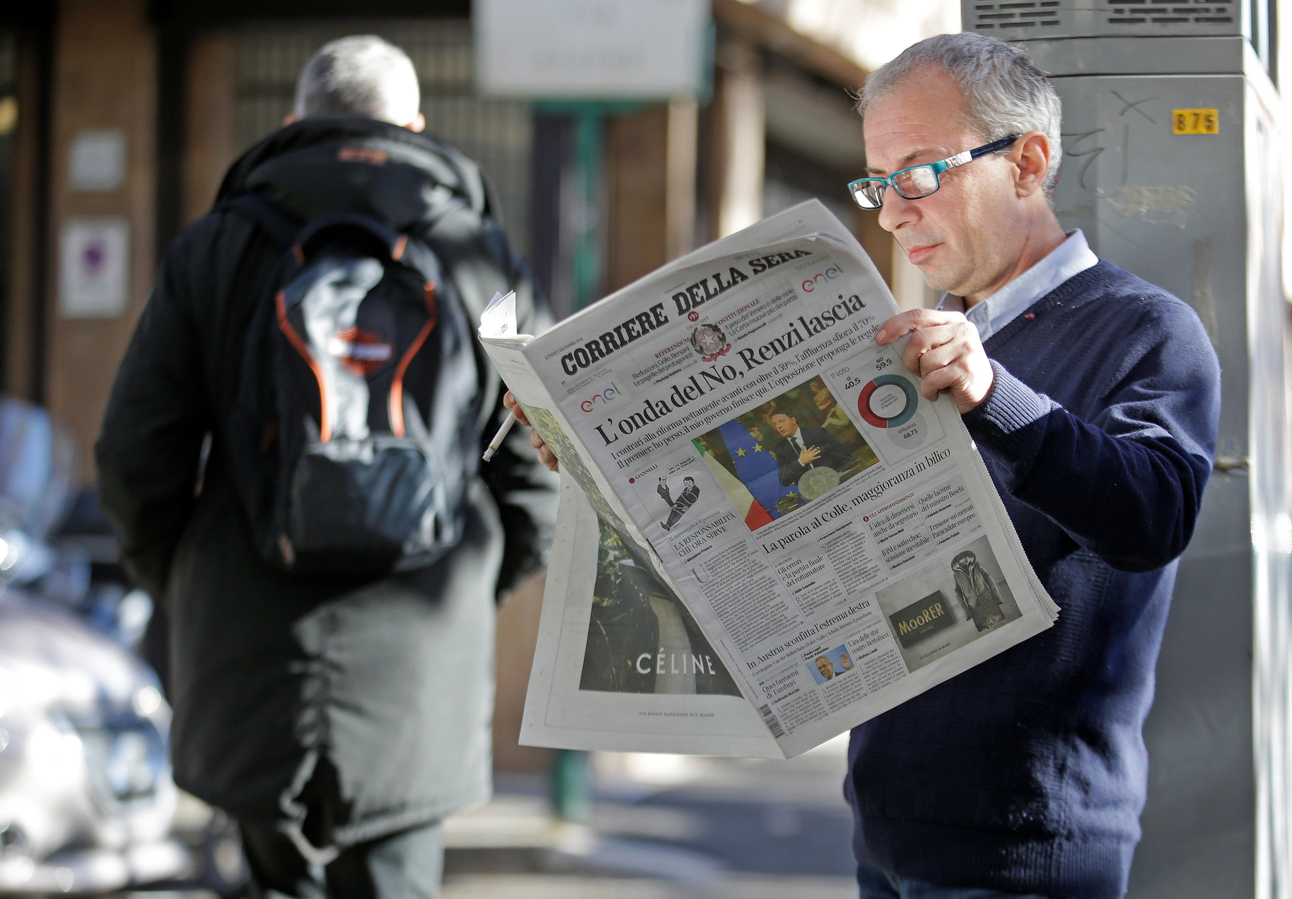 イタリアの首相の辞任報道を新聞で読む男性