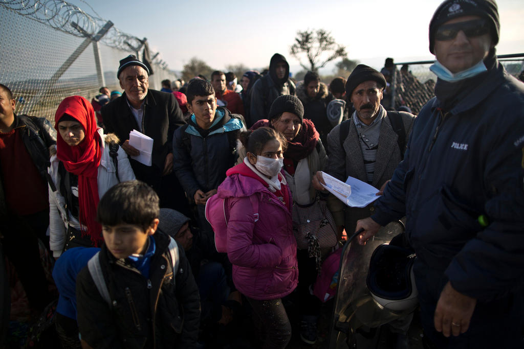 Profughi in attesa accanto a un poliziotto a Idomeni