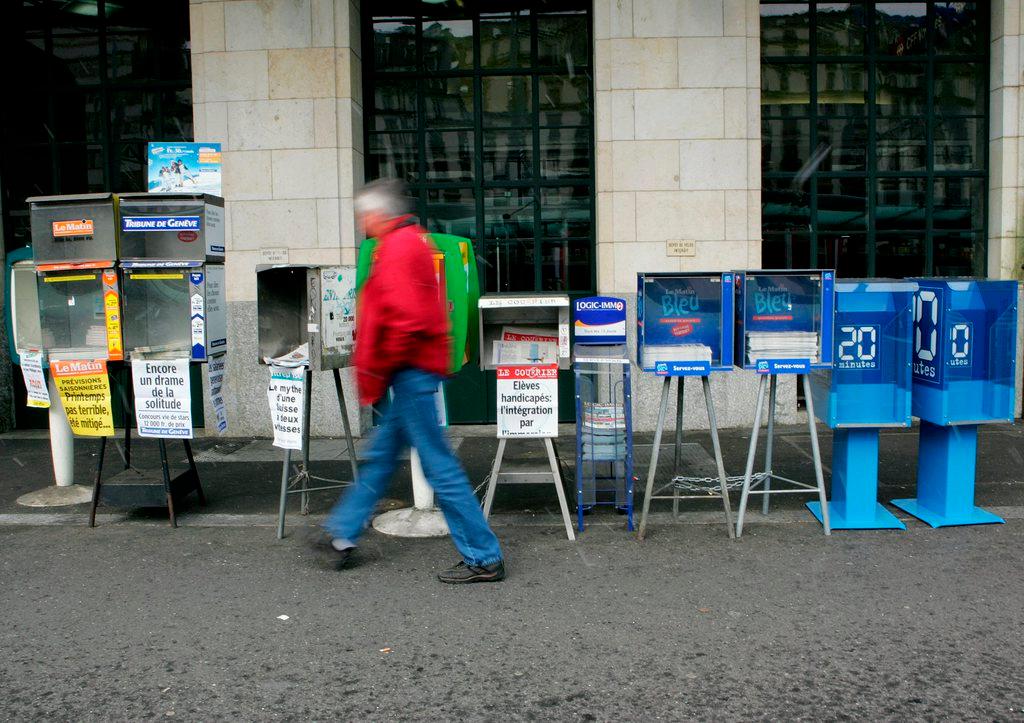 man walks past newspaper boxes