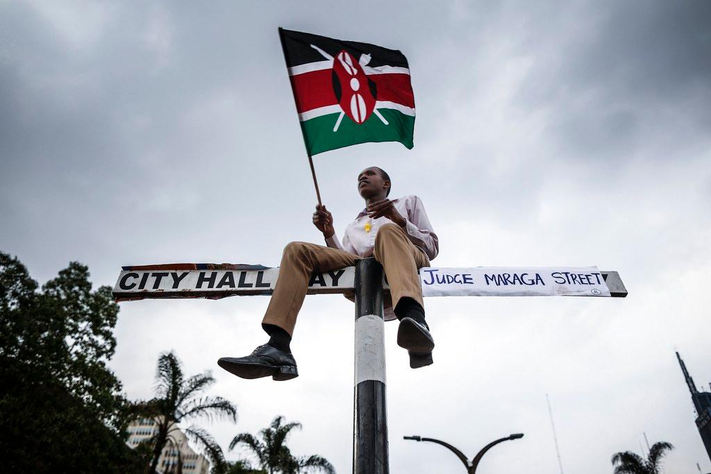 Manifestante kenyano arrampicato su un palo regge una bandiera del paese