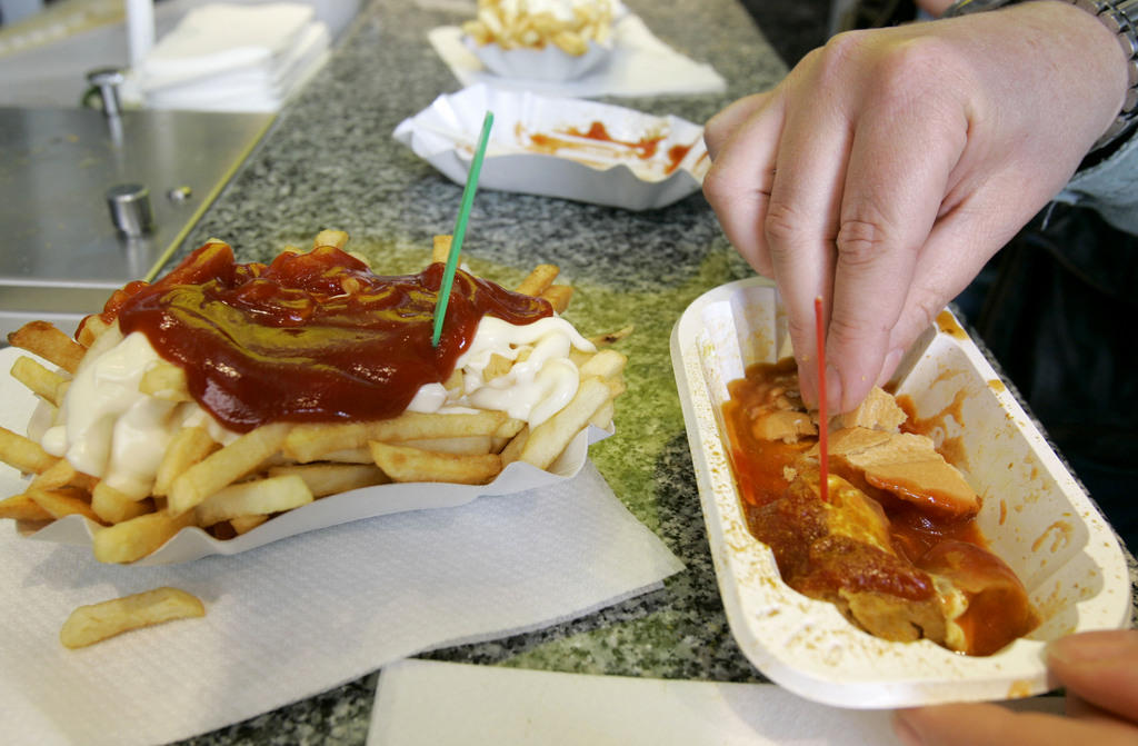 A hand takes a piece of sausage from a paper plate