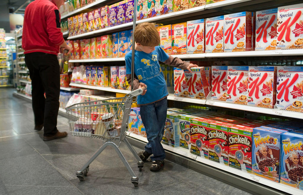 Un niño elige un paquete de cereales apilados en los estantes de un supermercado.